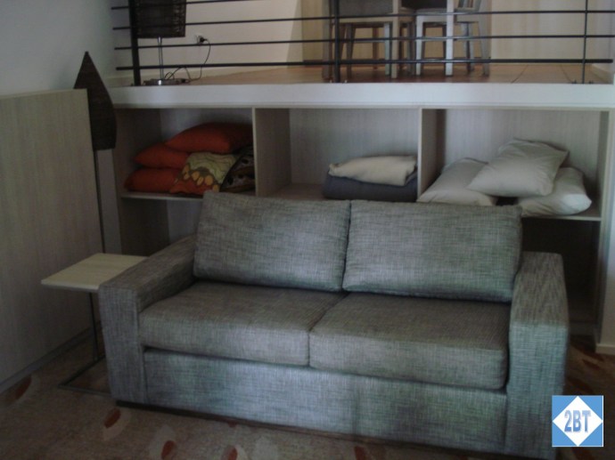 Love seat in the living area with extra bedding. Dining area on the level above the love seat.